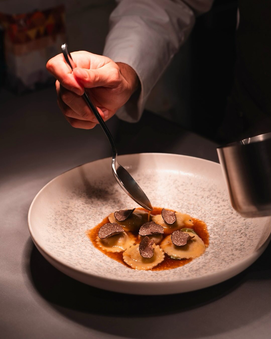 Focus on a white plate of ravioli, with the hand of the chef dropping sauce as the finishing touch of a gastronomic dish.