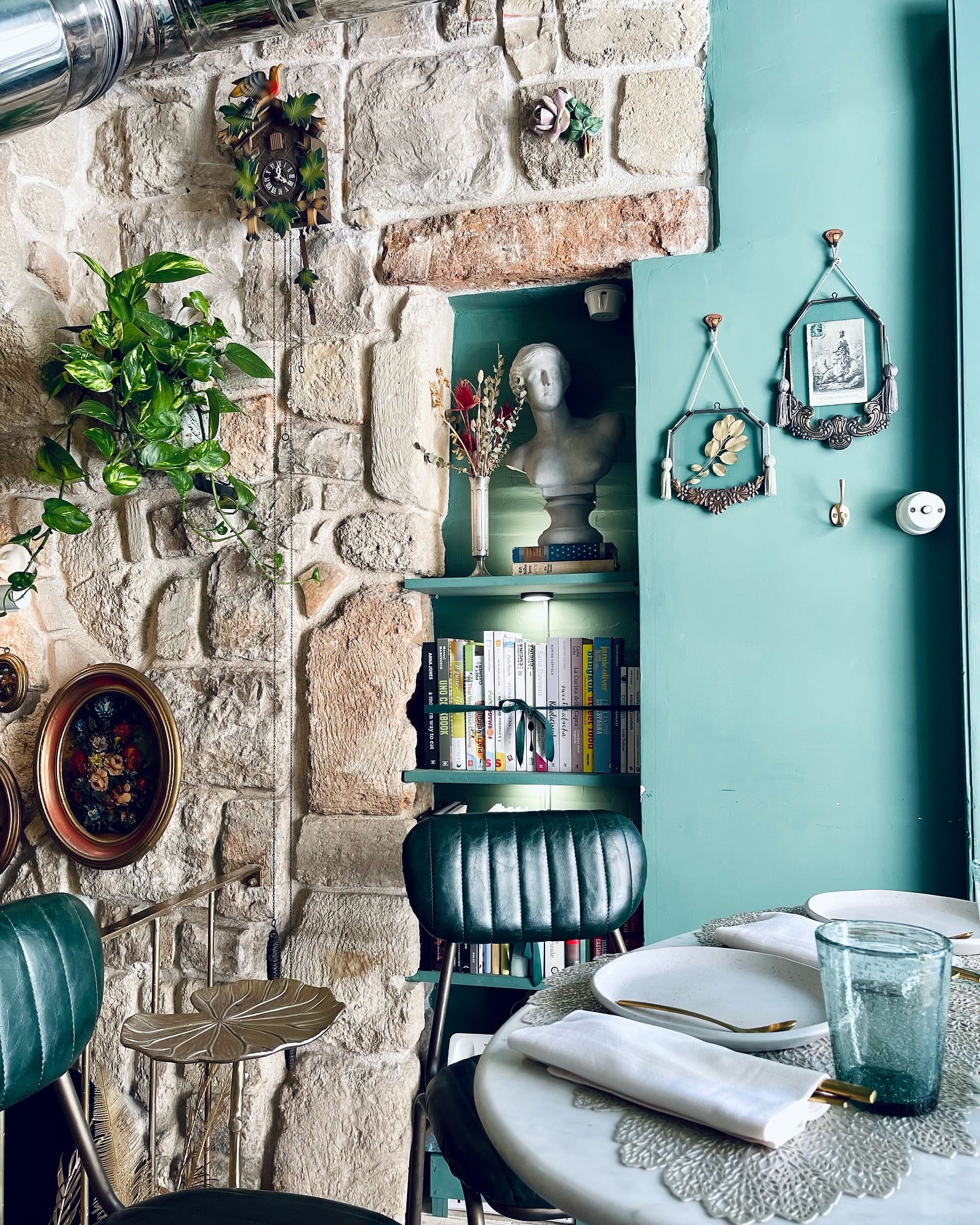 Closeup of a mint green wall, bricks, stones, books on shelves, a table and a plate